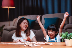 Two-girls-in-living-room-playing-dominos-on-coffee-table.-Younger-girl-triumphantly-raised-arms